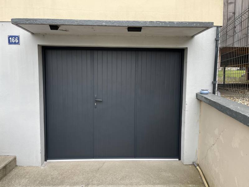 Artisan menuisier pour le remplacement d'une porte de garage en bois par une porte de garage en aluminium isolée en trois panneaux rainurés avec portillon de chez DC PRODUCTION, secteur FECAMP (76)